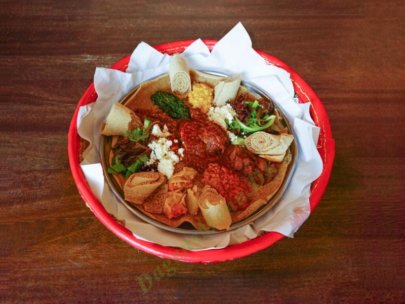 A shared platter of stews, salads and rolled injera on a red tray